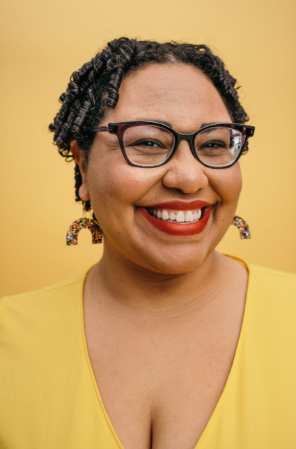 Photo of Dr. Sami Schalk a Black woman with curly hair, eyeglasses, rainbow earring and a big smile
